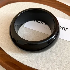 Detailed close-up of a thick minimalist glossy black resin bangle on a display card
