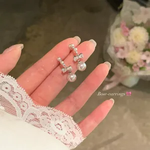 Macro view of dainty silver bow earrings with zircon stones and elegant white pearl drops