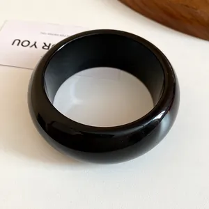 Detailed close-up of glossy black resin chunky bangle with a rounded minimalist design