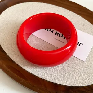 Close-up view of a vibrant red chunky resin bangle with a glossy finish on props.