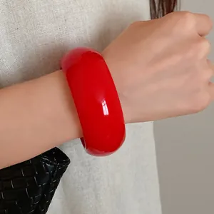 Close-up view of a vibrant wide red resin chunky bangle on wrist with minimalist design.