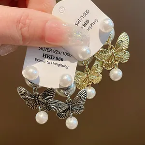 Close-up of butterfly earrings with white pearls in gold and silver finishes on cards.