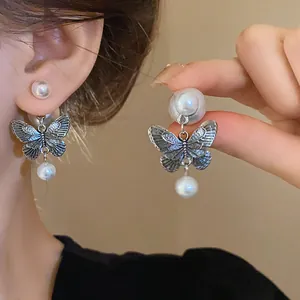 Close-up detail of vintage silver butterfly earrings with elegant white pearls on a model
