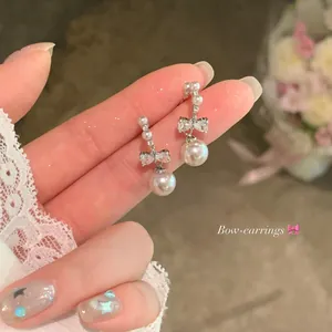 Detailed macro view of elegant silver bow-knot pearl stud earrings with zircons