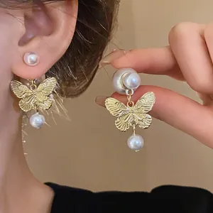 Close-up of elegant gold butterfly earrings with white pearl accents on a person's ear.