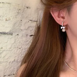Detailed view of elegant zircon bow earrings with a hanging pearl on model's ear