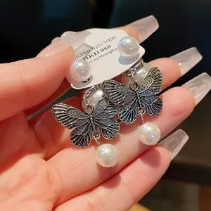Macro detail of silver butterfly stud earrings with dangling white pearl accents