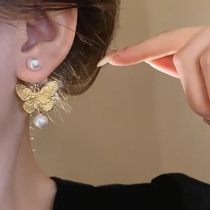Detailed macro view showing the elegant gold butterfly earrings with white pearl accents