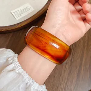 Dettaglio di un ampio bracciale retrò in acrilico ambrato sfumato indossato al polso, elegante