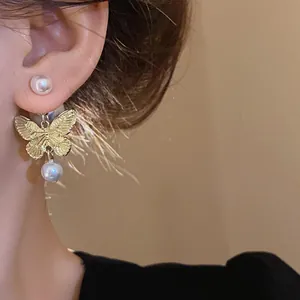 Close-up detail of elegant gold butterfly earring with pearl drop on ear.