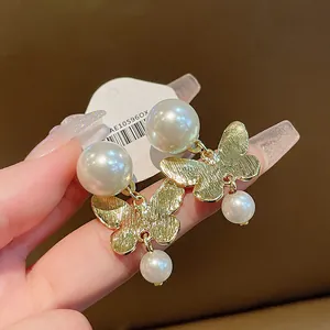 Close-up of golden butterfly earrings with large white pearls and drop details
