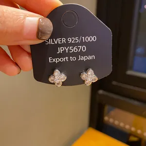 Silver four-leaf clover stud earrings pavé-set with clear stones on a display card