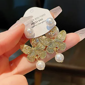 Close-up detail of golden butterfly pearl earrings with delicate engraved wing textures