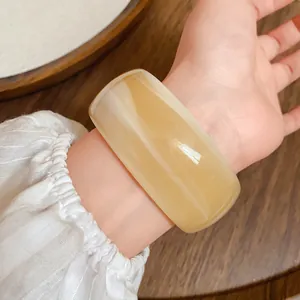 Vista dettagliata di un ampio bracciale in acrilico con motivo ambrato marmorizzato sul polso