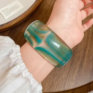 Primo piano di un ampio bracciale in acrilico marmorizzato con venature verde acqua e ambra