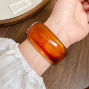 Primo piano di un ampio bracciale retrò in acrilico con trama marmorizzata ambra sul polso