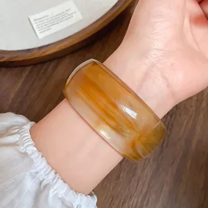 Primo piano di un ampio bracciale in acrilico con motivi ambrati sfumati sul polso.