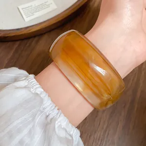 Primo piano di un ampio bracciale in acrilico marmorizzato ambra su un polso.