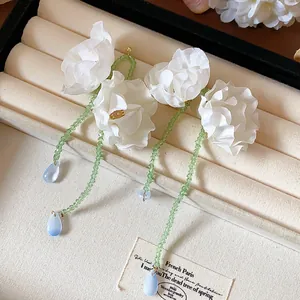 Close-up of white fabric flower tassel earrings with green beads and blue drops