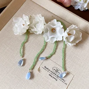 Close-up of white fabric flower earrings with green bead tassels and blue drops