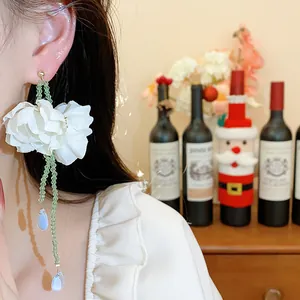 Detailed close-up of elegant white fabric flower earrings featuring green bead tassels on a model