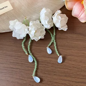 Detailed view of elegant white fabric flower tassel earrings with green crystal beads