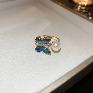 Gros plan d'une bague papillon plaquée or avec des ailes en nacre et une perle blanche