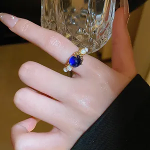 Gros plan d'une bague d'index dorée avec perle bleue et détails de perles d'eau douce.