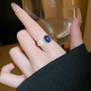 Gros plan d'une bague plaquée or avec une perle blanche et une pierre bleue au doigt.