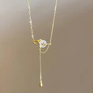 Detailed close-up of a golden snake necklace with white jade-like ring and teardrop charm