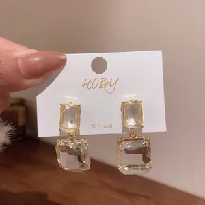 Detailed macro shot of geometric transparent square drop earrings with gold-tone metal frame.