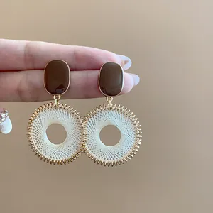 Close-up of retro woven round drop earrings with brown oval studs.