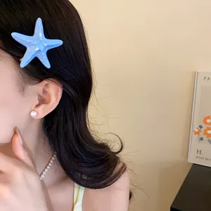 Nahaufnahme einer blauen Seestern-Haarklammer kombiniert mit eleganten Perlenohrringen am Model