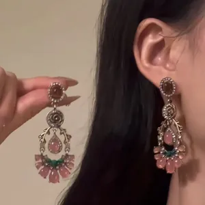 Close-up view of vintage floral dangle earrings with pink resin stones and intricate detail.