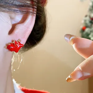 Close-up detail of red enamel horse stud earring worn on ear with a festive background