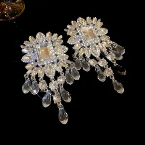 Detailed close-up of exaggerated silver earrings with square crystals and long tassels.