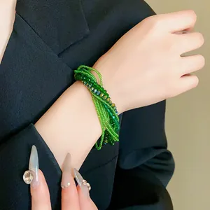 Close-up of multi-layer green crystal seed bead bracelet on female wrist over black blazer.