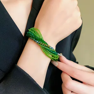 Close-up of a multi-layer green seed bead and crystal bracelet worn on a woman's wrist.