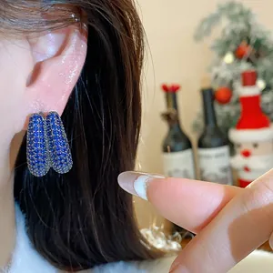 Close-up view of elegant blue zircon geometric hoop earrings worn on ear in festive setting