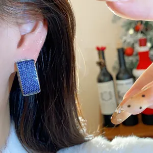 Close-up view of elegant geometric earrings with sparkling blue zircons worn on ear profile