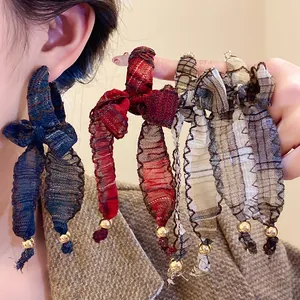 Close-up detail of plaid fabric bowknot tassel earrings with elegant gold beads.