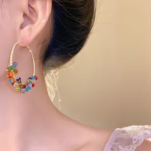 Primo piano di un orecchino a cerchio avvolto in perline di vetro colorate su una modella.