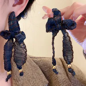 Detail view of blue fabric bow tassel earrings with gold beads and denim texture