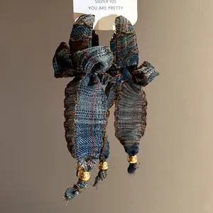 Detail shot of vintage plaid fabric bow earrings with gold beads and a silver tag