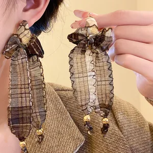 Detailed close-up of vintage plaid fabric bow tassel earrings with decorative gold bead accents