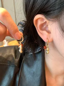 Close-up detail of stylish golden peanut hoop earrings with elegant red glass beads on ear