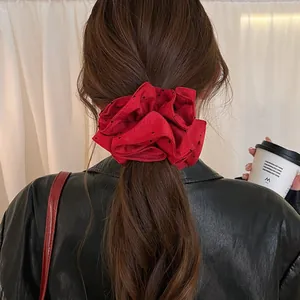 Close-up detail of an oversized red polka dot scrunchie worn on a ponytail styling