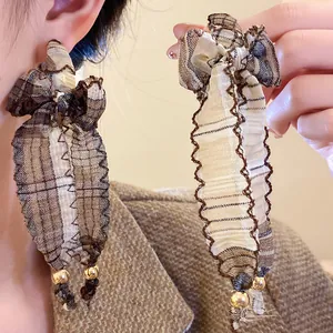 Macro detail view of vintage plaid fabric bow tassel earrings decorated with gold bead accents