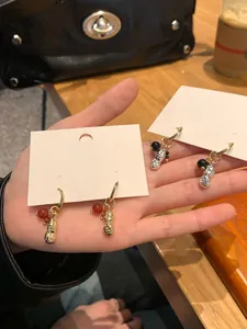 Close-up of elegant peanut-shaped hoop earrings with red and black glass bead charms.