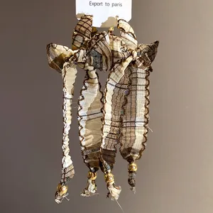Macro view of vintage plaid fabric bow tassel earrings with elegant gold beads